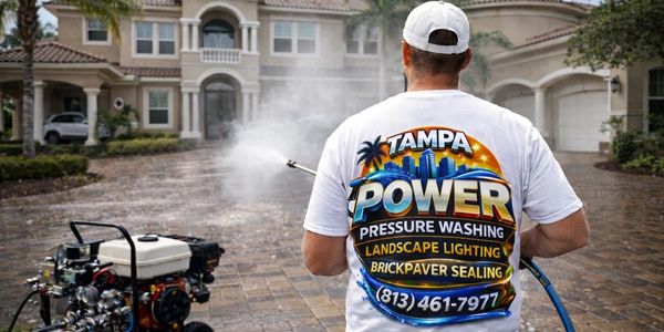 Person pressure washing a driveway in front of a large house.