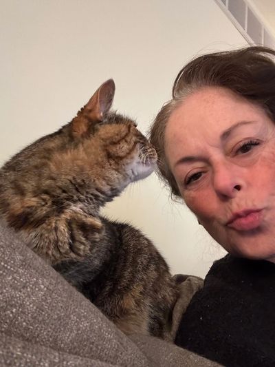 Woman puckering lips while a tabby cat looks away beside her.