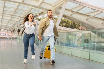 Happy couple running through an airport with luggage.