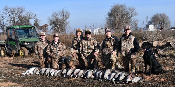 Group of hunters with their duck hunting catch and a black dog outdoors.