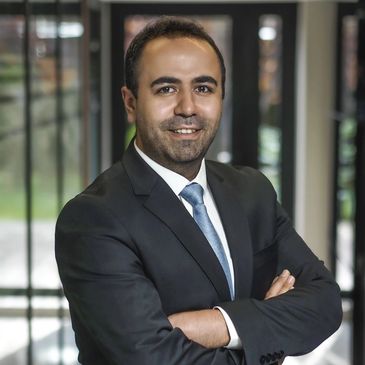 Confident man in a suit smiling with arms crossed indoors.