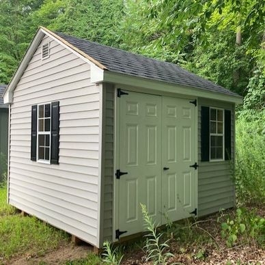 A small beige garden shed with double doors and black shuttered windows.