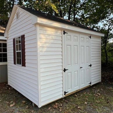 Small white storage shed with double doors and brown shutters.
