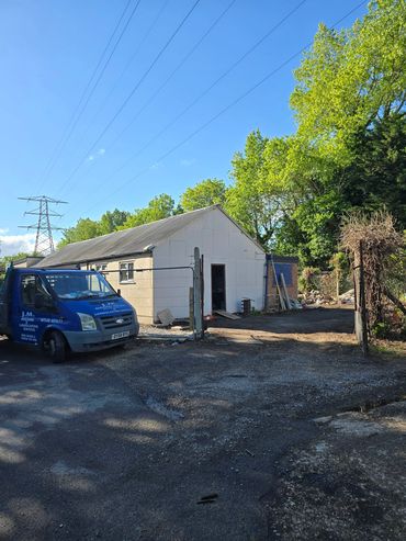 A blue van parked beside a white building under construction with trees and power lines.