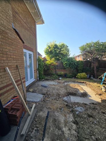Backyard under construction with bricks, soil, and garden plants in the background.