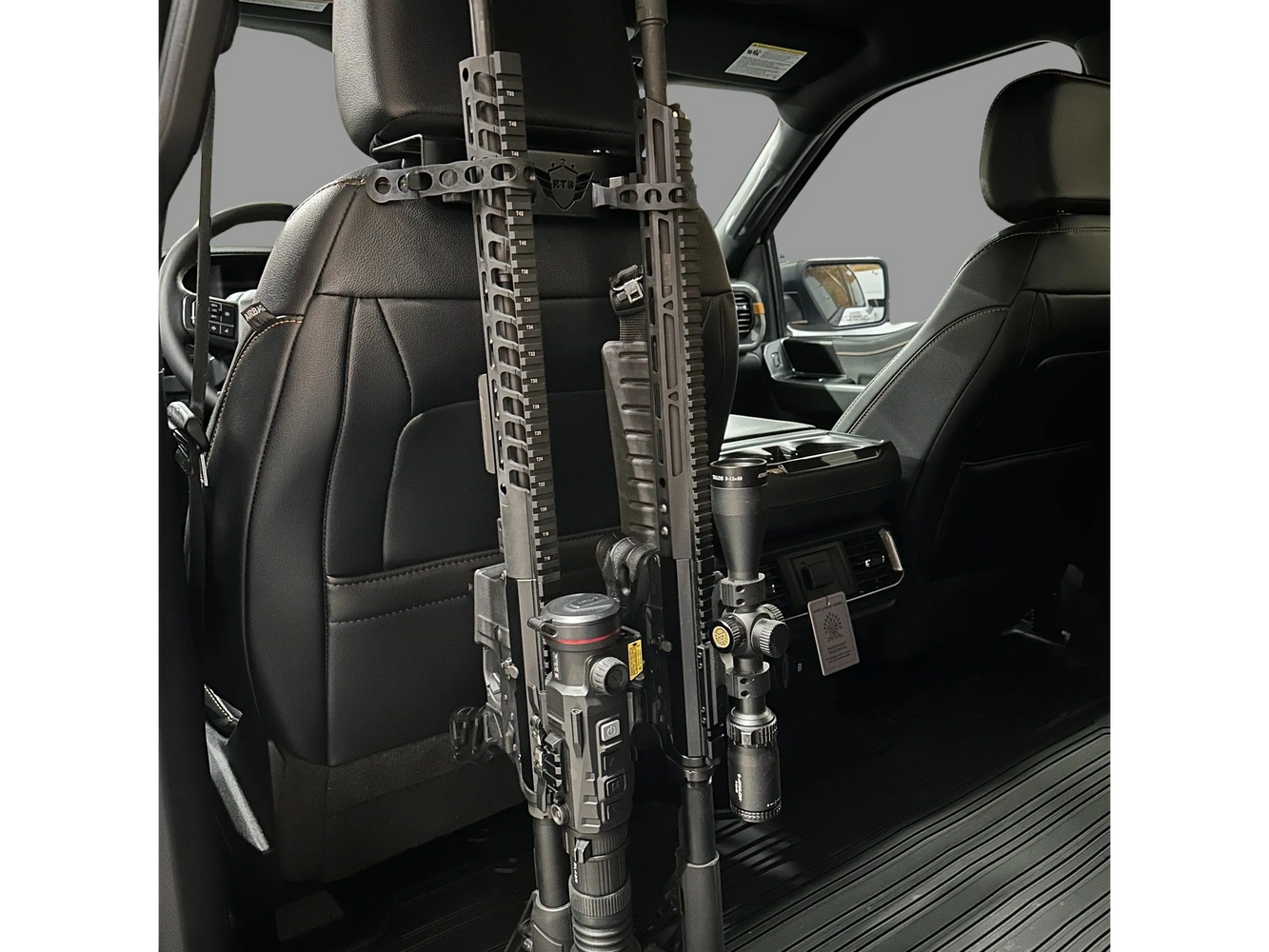 Two rifles mounted on the back of a car seat headrest inside a vehicle.