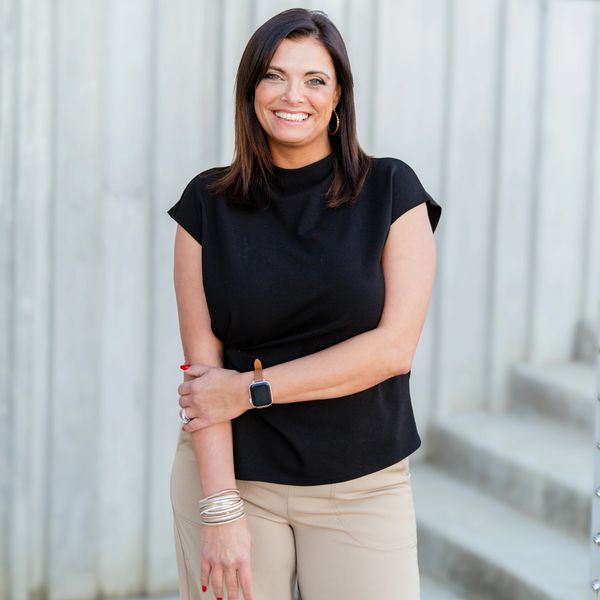 Smiling woman in black top and beige pants standing outdoors.