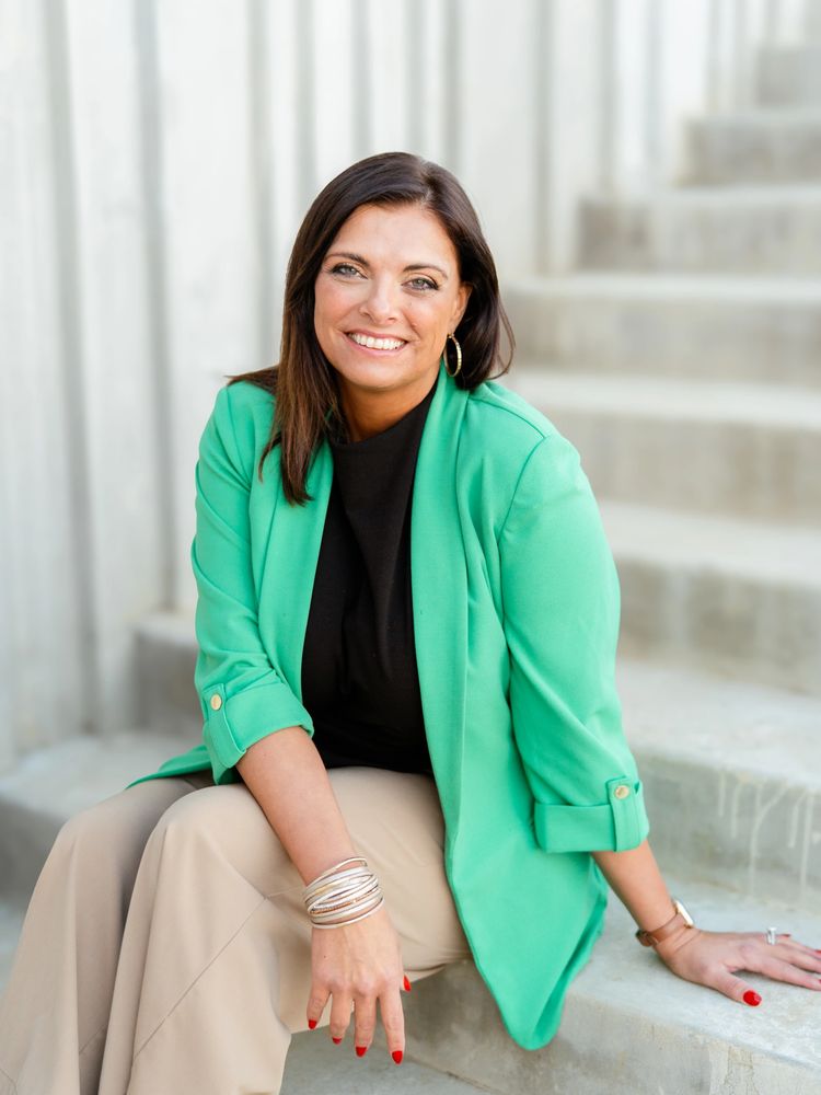 Smiling woman in a green blazer sitting on concrete steps.