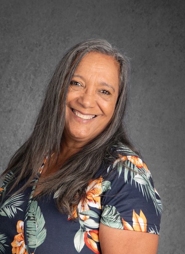Smiling woman with long gray hair in floral shirt against gray background.