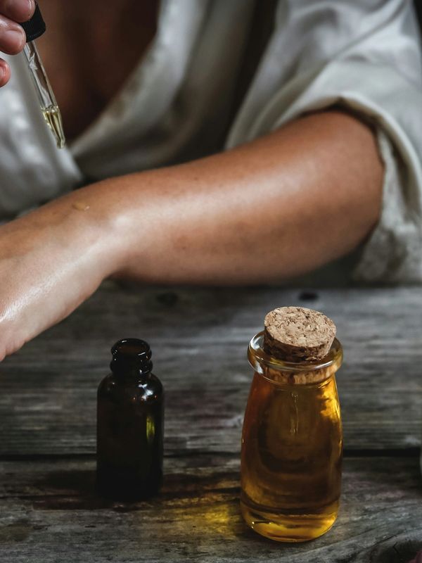 Person applying essential oil on arm with dropper and bottles on table.