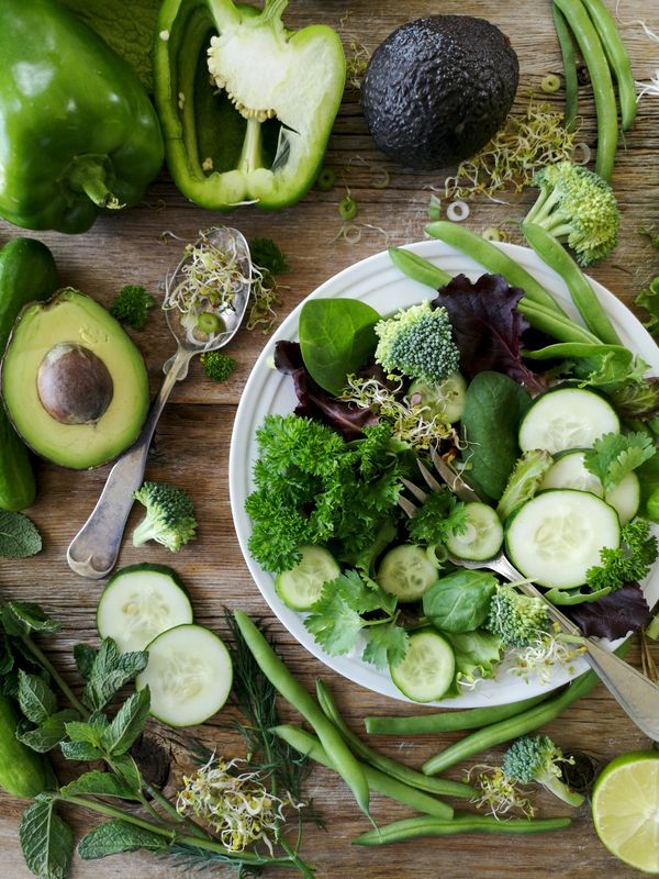Fresh green salad with avocado, cucumber, and herbs on a wooden table.