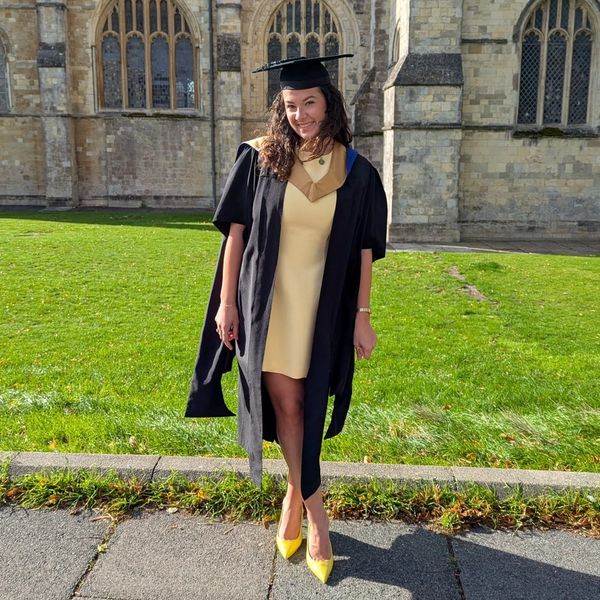 Woman in graduation gown and cap posing outside a historic building.