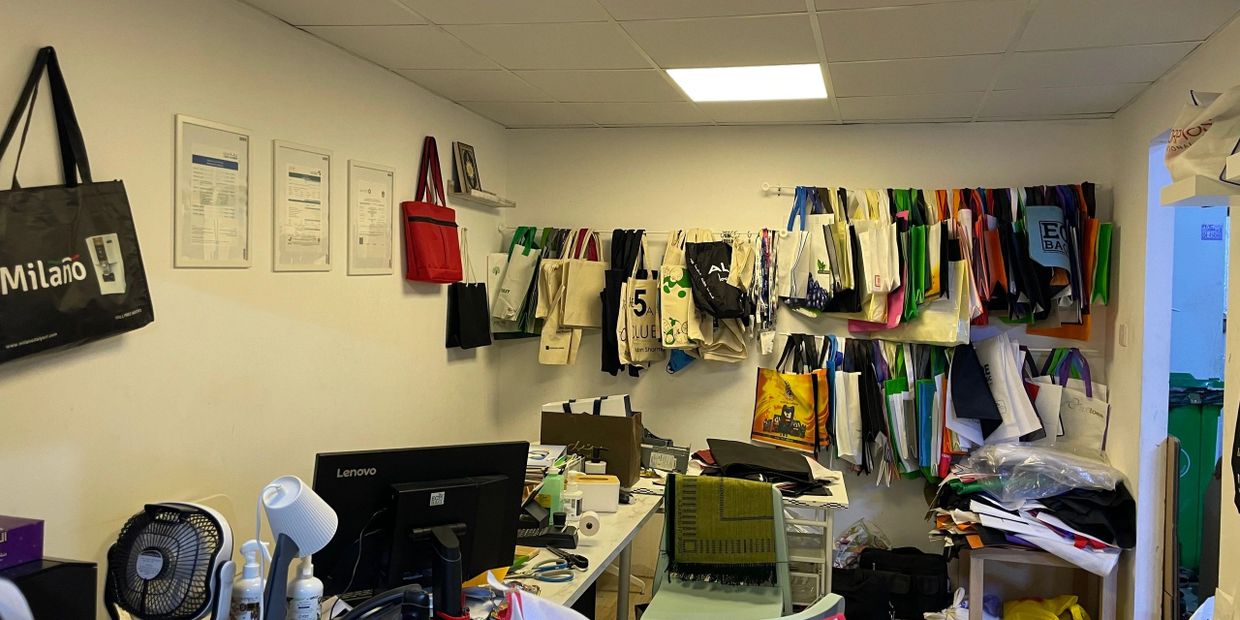 A workspace with bags hanging on the wall and a cluttered desk.