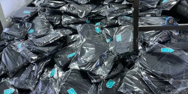 A large pile of black garments individually wrapped in plastic packaging.