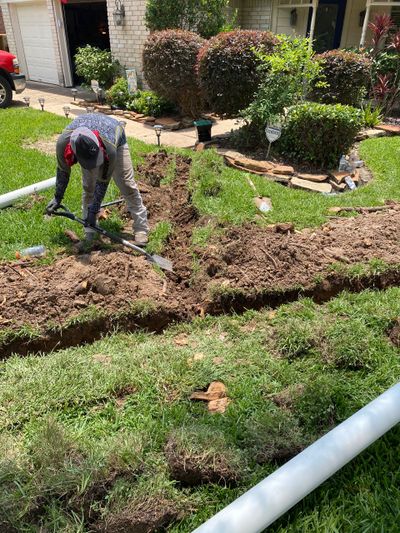 Person digging a trench in a garden with landscaping around.