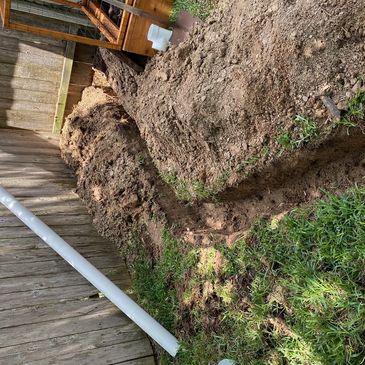 A trench dug alongside a wooden fence in a backyard.