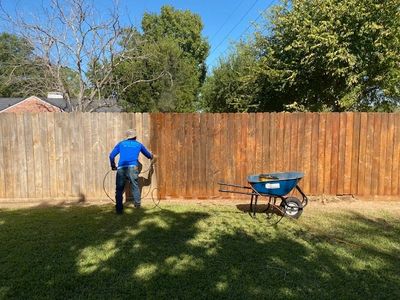 Person staining a wooden fence with a spray tool on a sunny day.