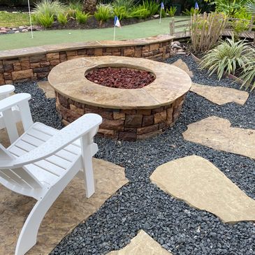 Stone fire pit with white chair and stepping stones in landscaped backyard.