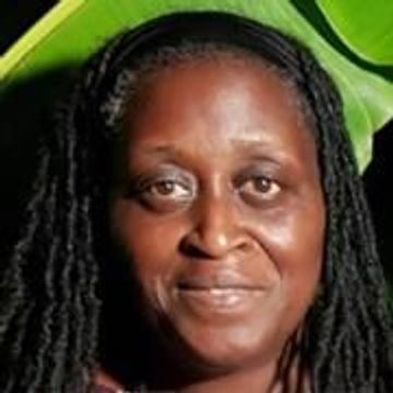 Portrait of a smiling woman with long braided hair and a green leafy background.