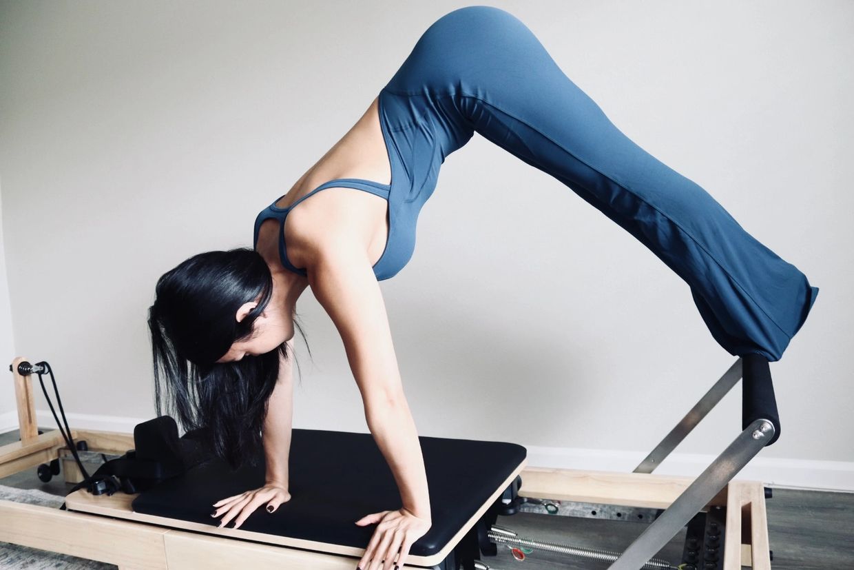 Woman in blue workout clothes doing Pilates on a reformer machine.
