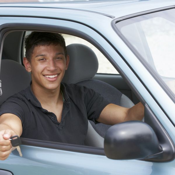 Smiling young man sitting in a car holding out a key.