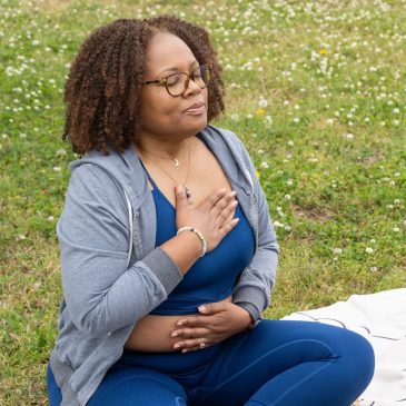 Woman meditating outdoors with hands on chest and belly.