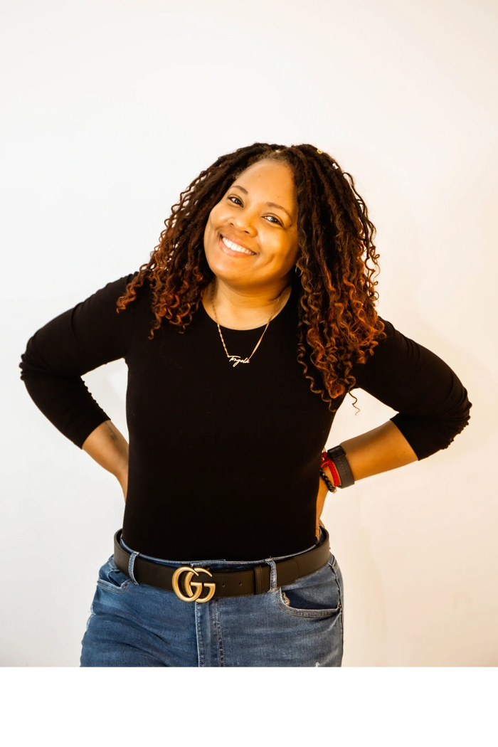 Smiling woman with curly hair, wearing a black top and jeans, posing confidently.