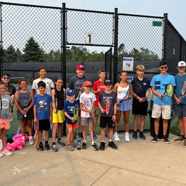 Group of children and teens holding tennis rackets posing on a tennis court.