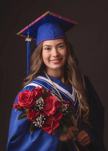 Young woman in graduation attire holding a bouquet of red roses.