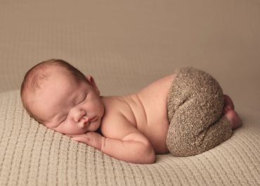 Newborn baby peacefully sleeping in cozy knitted pants on a soft beige blanket.