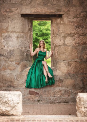 Woman in a flowing green dress sitting in a stone window frame.
