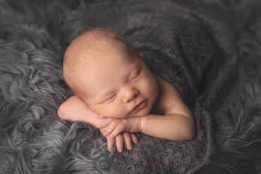 Newborn baby peacefully sleeping on a soft gray blanket.