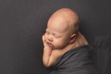 Sleeping newborn baby wrapped in a dark cloth.