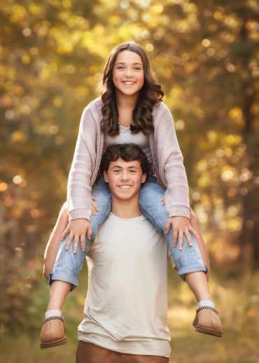 Smiling siblings enjoying a piggyback ride outdoors in autumn.