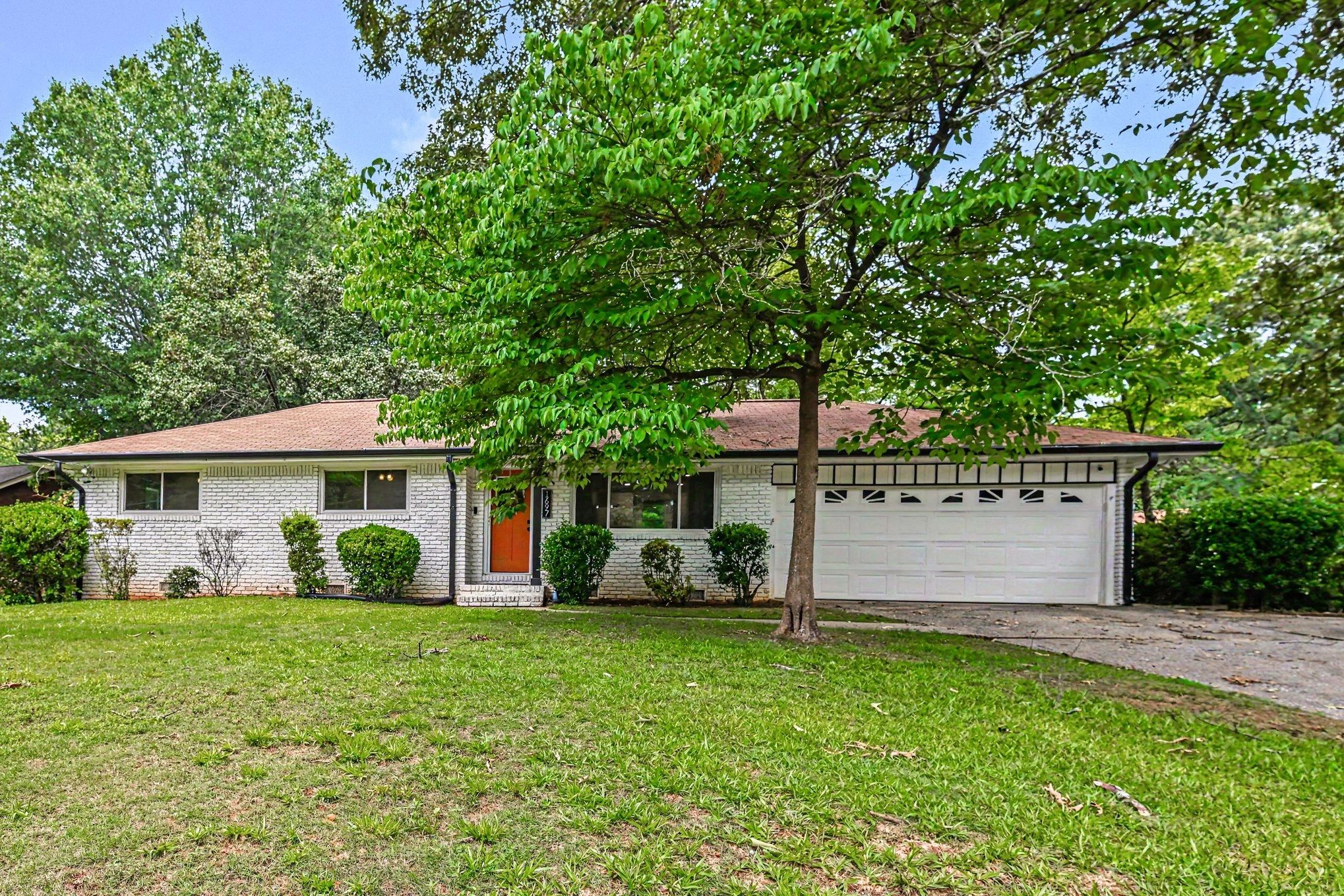White brick ranch with a red door and large tree in front.