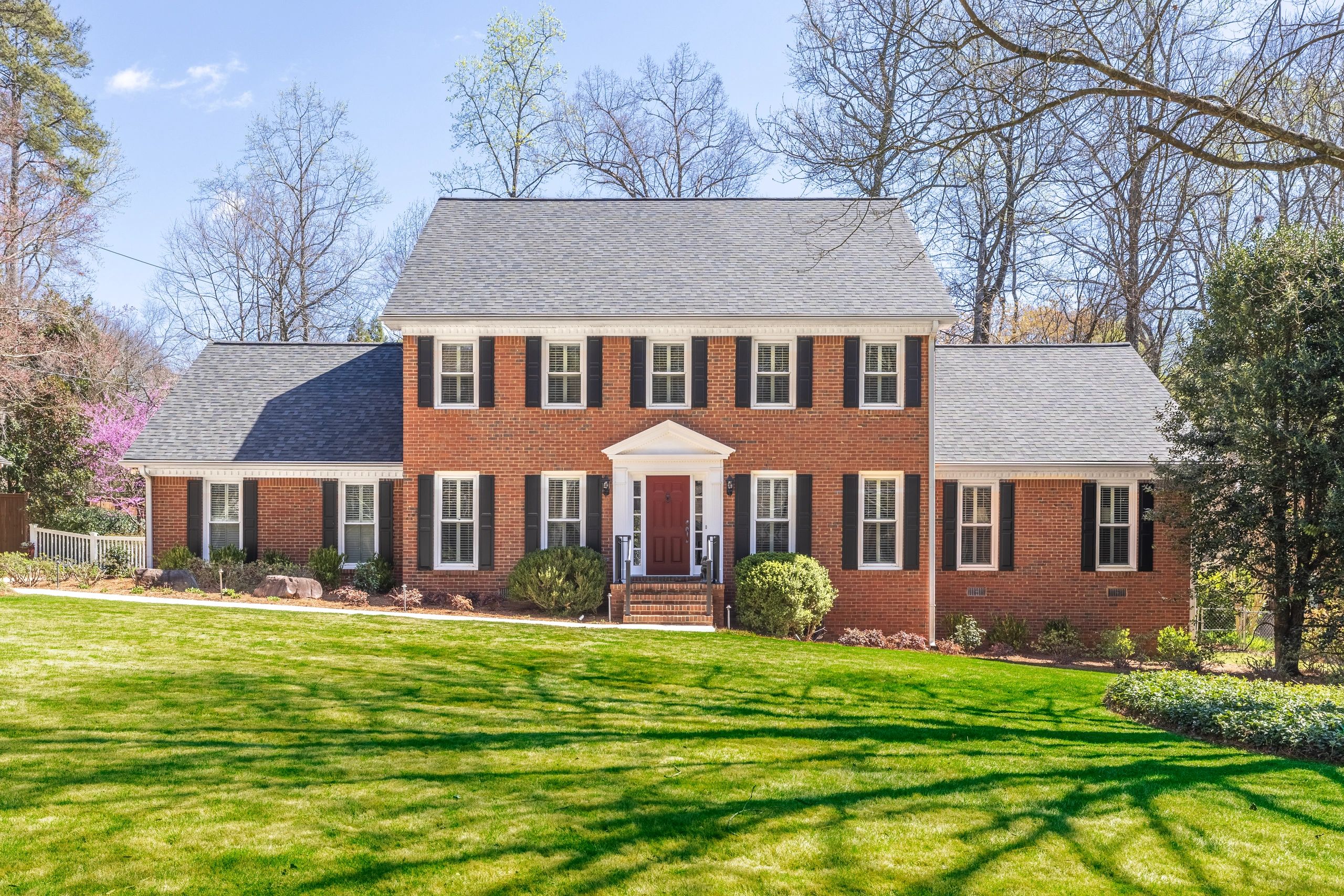 Classic brick house with black shutters and a red door on a sunny day.