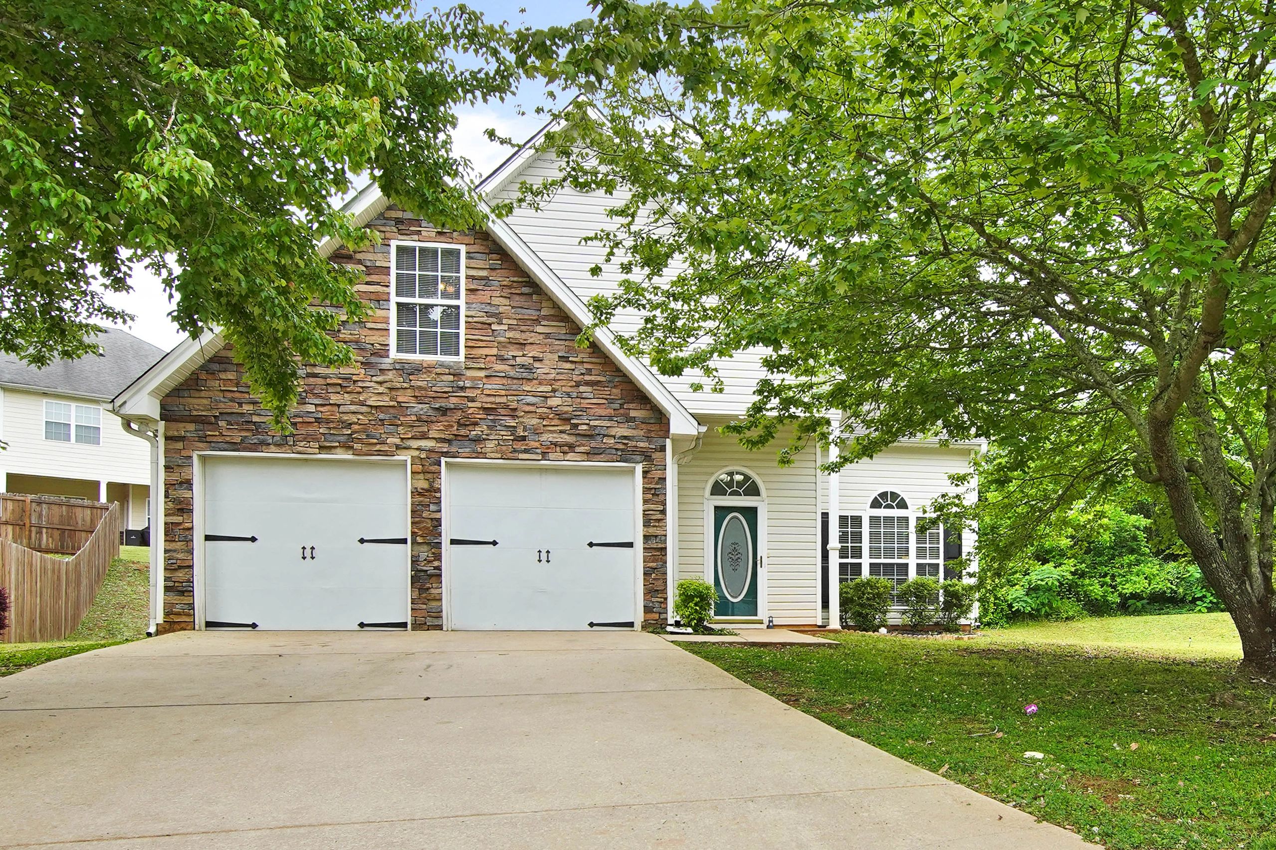 Suburban house with stone facade, double garage, and lush green trees.
