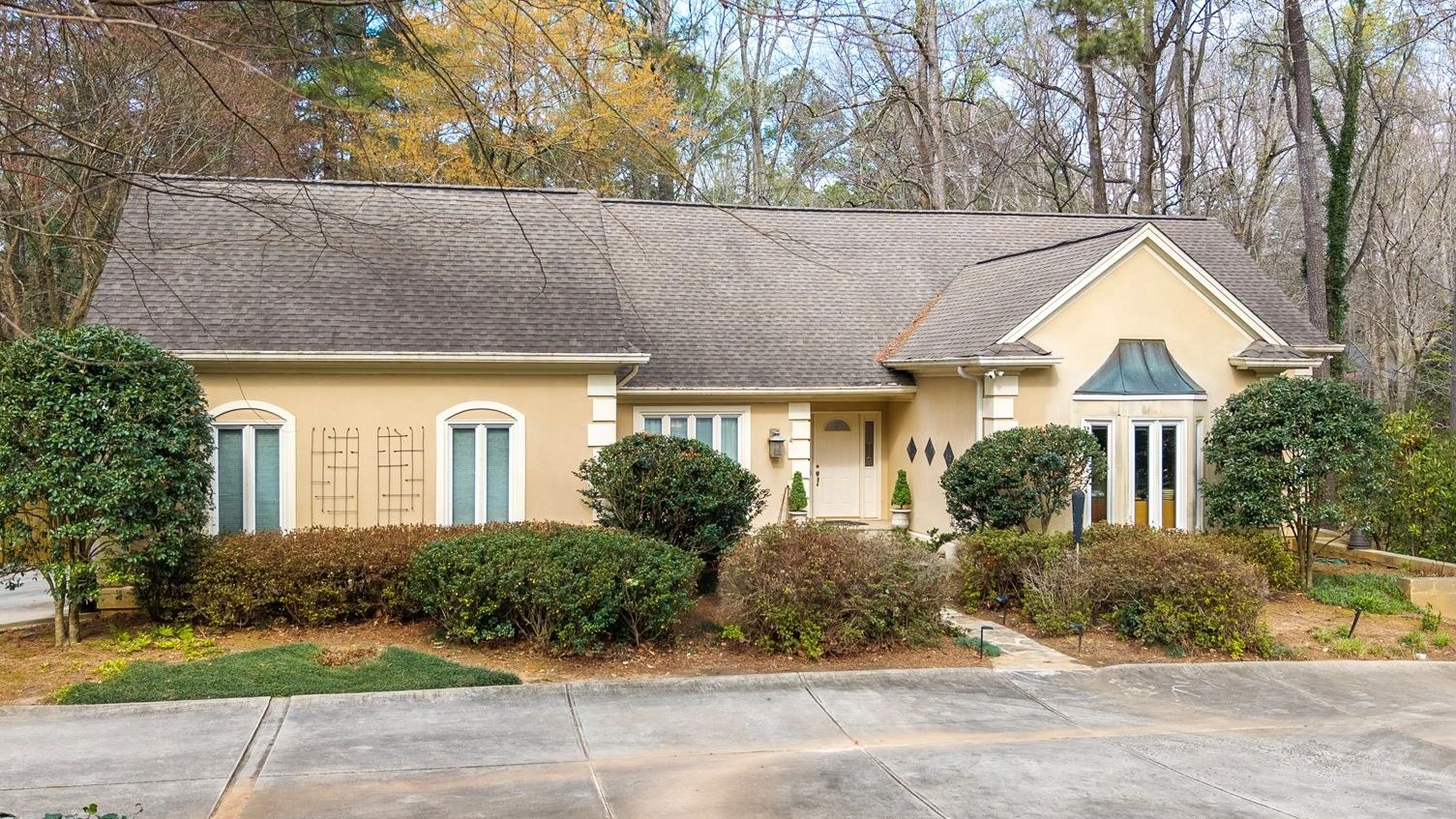 Single-story beige house with manicured bushes and a concrete driveway.