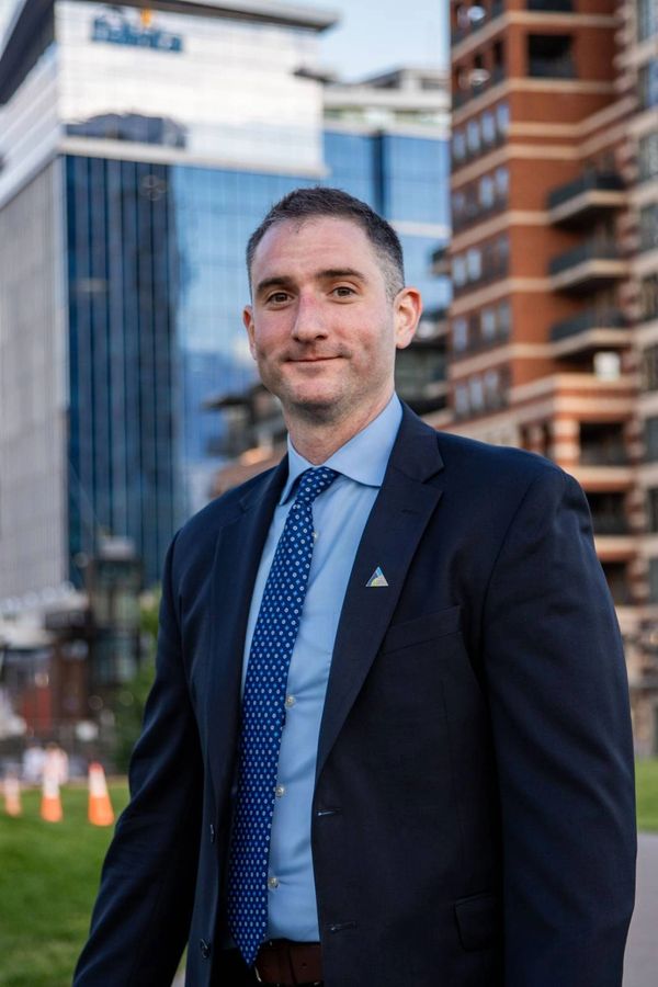 Man in a suit standing outdoors with buildings in the background.