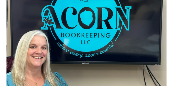 Smiling woman sitting in front of a screen with Acorn Bookkeeping logo.