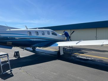 A person cleaning the wing of a small private airplane on a sunny day.