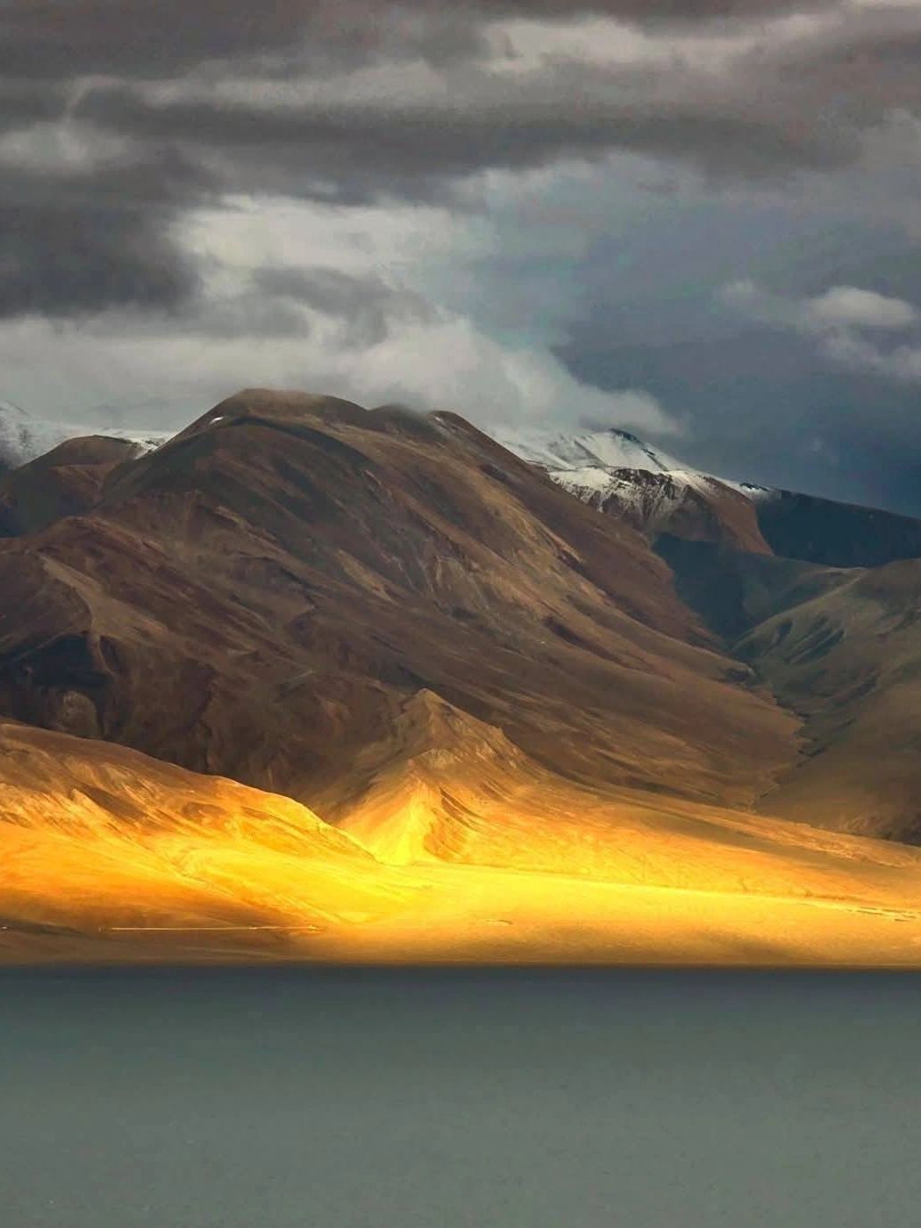 Golden sunlight illuminates a mountain range under cloudy skies.