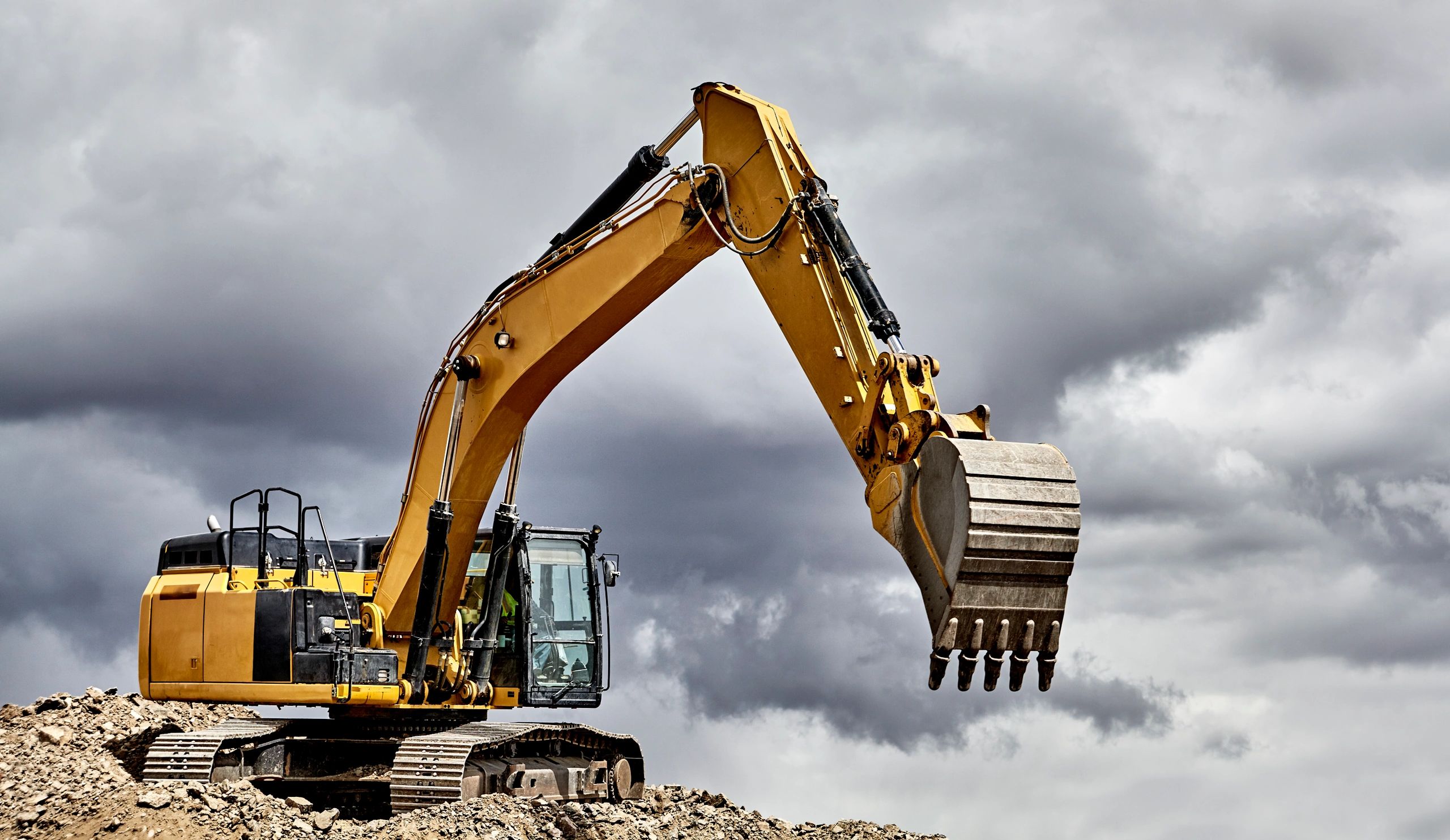 Yellow excavator on rocky ground against a cloudy sky.