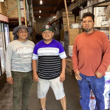 Three men standing in a warehouse with shelves and boxes around them.