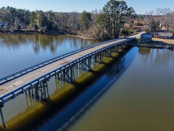 A long wooden bridge over calm water leading to a wooded area.