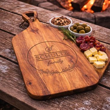 Personalized wooden cutting board with snacks by a campfire.