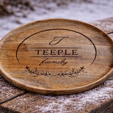 Wooden plate engraved with 'T' Teeple family' on snowy wooden surface. Custom designs creating unique, one of a kind items for everyday use.