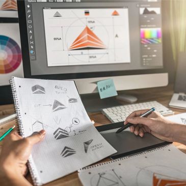 Designers sketching and digitizing logo concepts on a tablet and computer.
