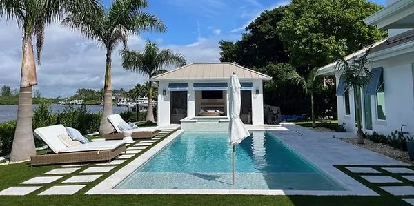 Modern backyard with a pool, lounge chairs, and palm trees under a blue sky.
