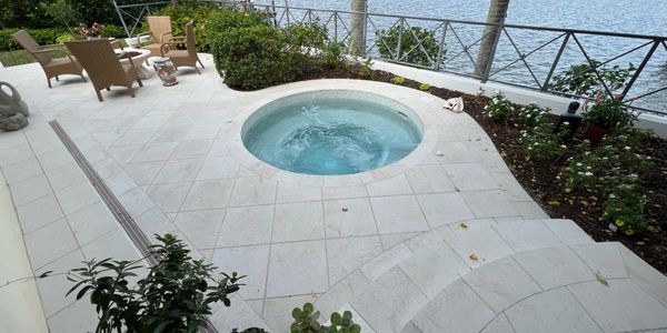 Outdoor patio with round hot tub and seating overlooking water.